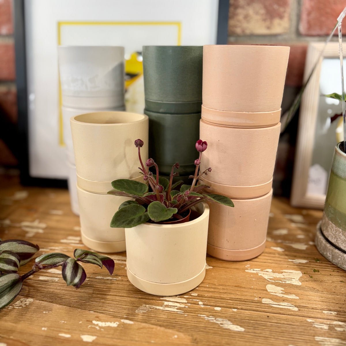 Earth tone planters stacked on a wooden surface with a blurred indoor setting at Paisley Gardens in Northfield, MN.