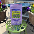 A bag of Coast of Maine Organic & Natural Rhododendron, Azalea & Berry garden mix stands on a green metal plant stand outdoors, surrounded by potted flowers at Paisley Gardens in Northfield, MN.