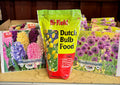 A bag of Hi-Yield Dutch Bulb Food fertilizer standing on a wooden shelf, flanked by bulb packets for Hyacinth and Allium varieties at Paisley Gardens in Northfield, MN.