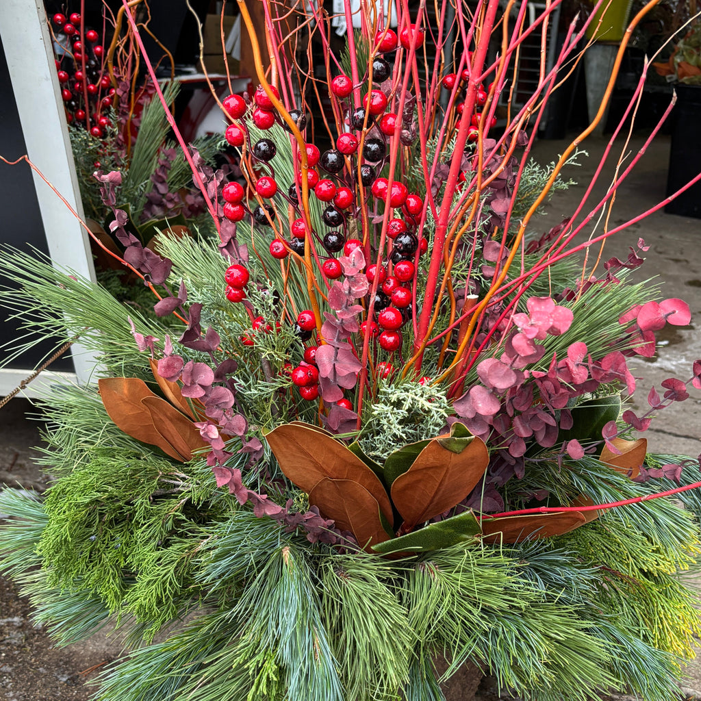 A festive holiday  arrangement featuring green pine needles, brown magnolia leaves, pink eucalyptus, bright red berries and red dogwood stems at Paisley Gardens in Northfield, MN.