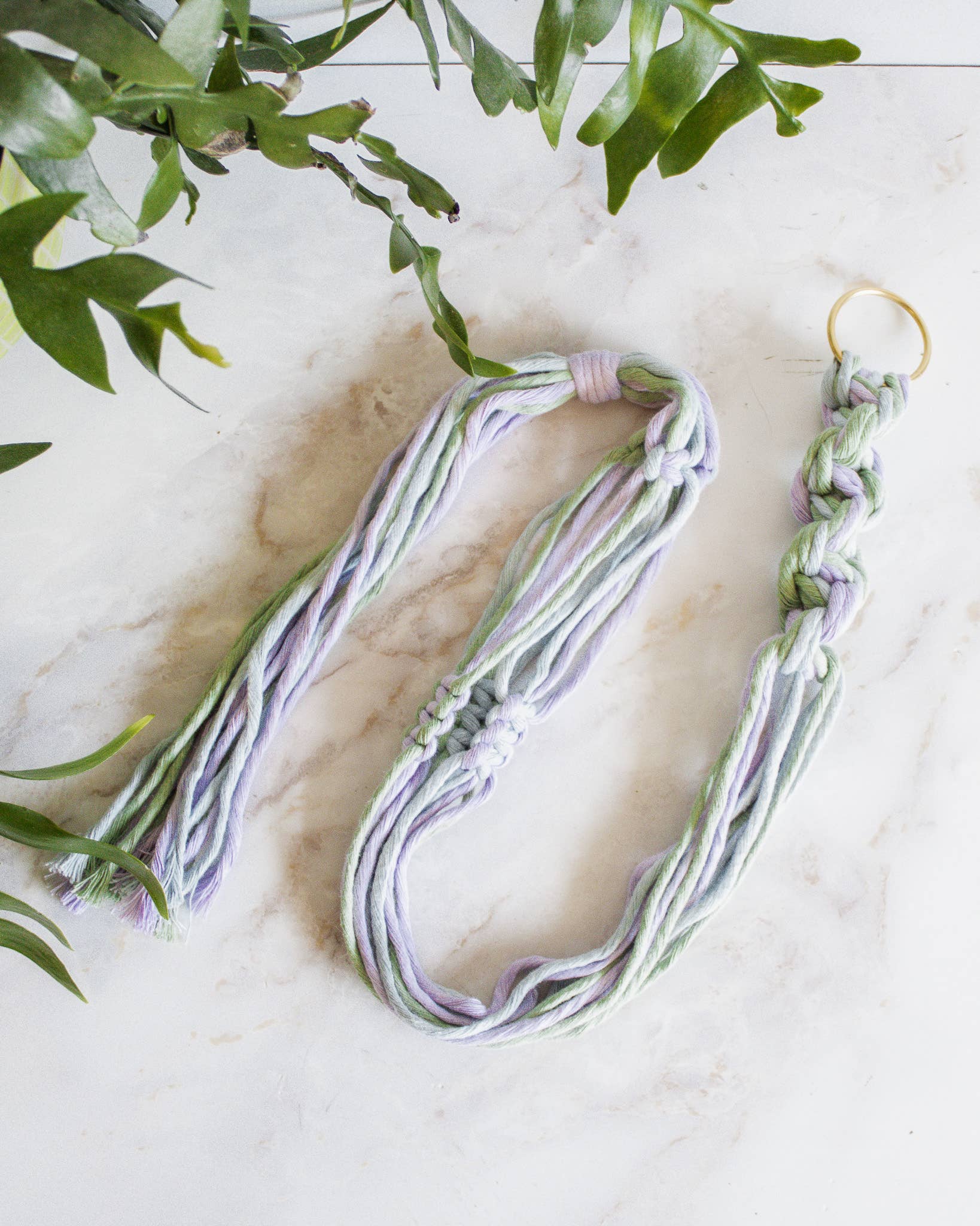 Braided macrame plant hanger on a marble surface with green leaves at Paisley Gardens in Northfield, MN.