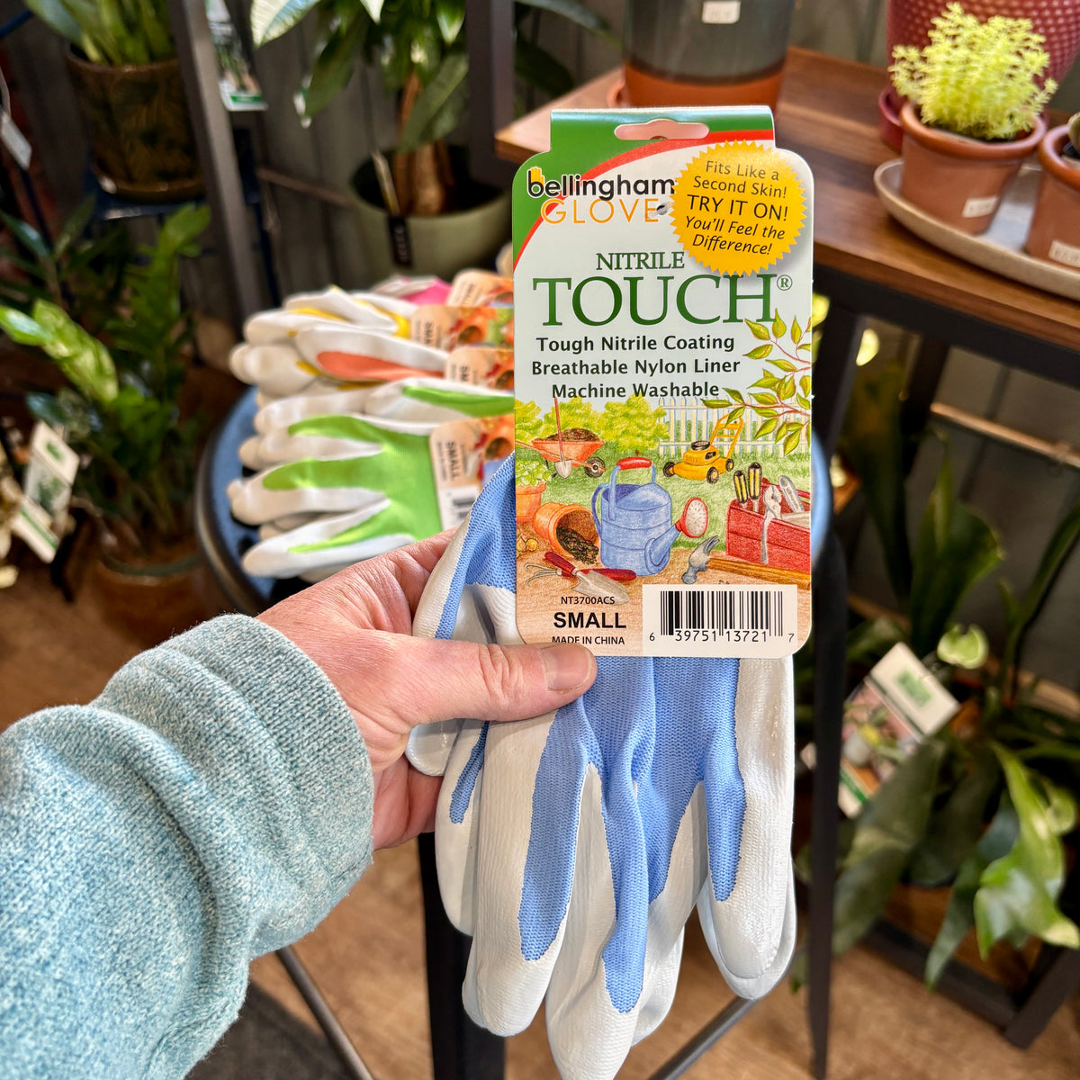 A hand holding a pair of Nitrile Touch blue gardening gloves in size small at Paisley Gardens in Northfield, MN.