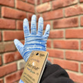 A hand modeling a blue and white textured gardening glove in front of a blurred brick background at Paisley Gardens in Northfield, MN.